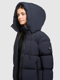 Model trägt dunkelblaue Steppjacke mit hochgezogener Kapuze und Reißverschlusstaschen.