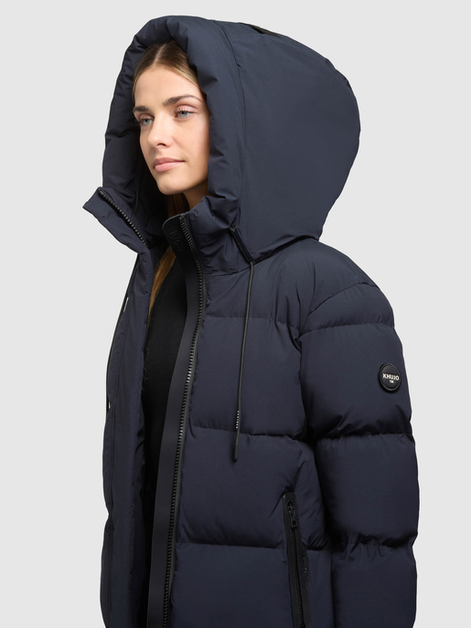 Model trägt dunkelblaue Steppjacke mit hochgezogener Kapuze und Reißverschlusstaschen.