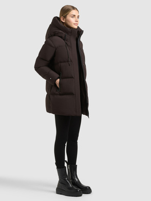 Model trägt dunkelbraunen, wattierten Parka mit Kapuze, schwarzen Leggings und Stiefeletten.