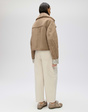 Rückansicht einer braunen Velourslederjacke mit hellem Teddyfutter, getragen zu cremefarbener Jeans.