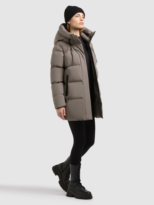 Model trägt einen taupefarbenen Steppmantel mit Kapuze und schwarzer Rippmütze.