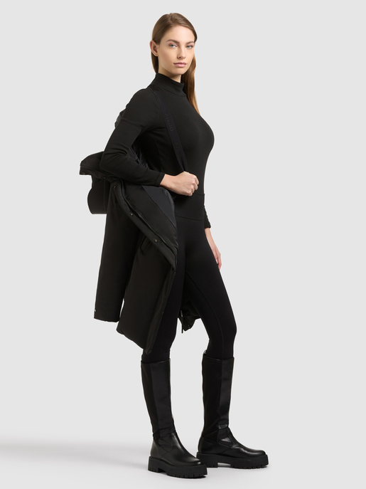Model trägt einen schwarzen Overall mit Stehkragen und hält einen schwarzen Rucksack.