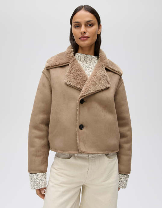 Model trägt eine beigefarbene kurze Jacke in Velourslederoptik mit breitem Teddyfutter-Kragen und dunklen Knöpfen.