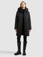 Model trägt schwarzen langen Parka mit Kapuze und Reißverschluss.