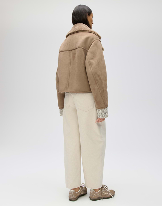 Rückansicht einer braunen Velourslederjacke mit hellem Teddyfutter, getragen zu cremefarbener Jeans.