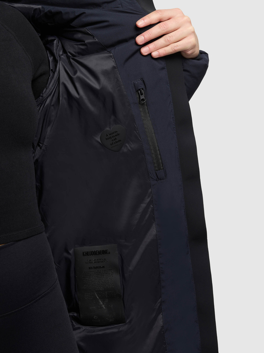 Detailansicht des Innenfutters einer dunkelblauen Jacke mit Reißverschlusstasche und Markenlabel.