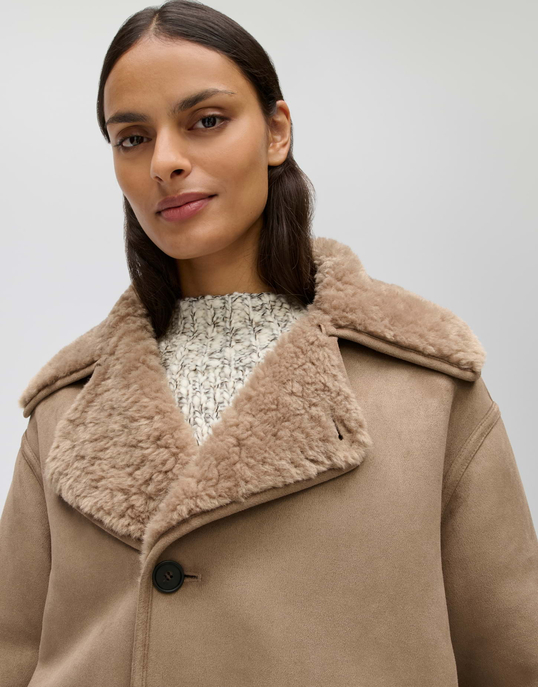 Model trägt beigen Mantel mit breitem Kunstfellkragen und schwarzem Knopf.